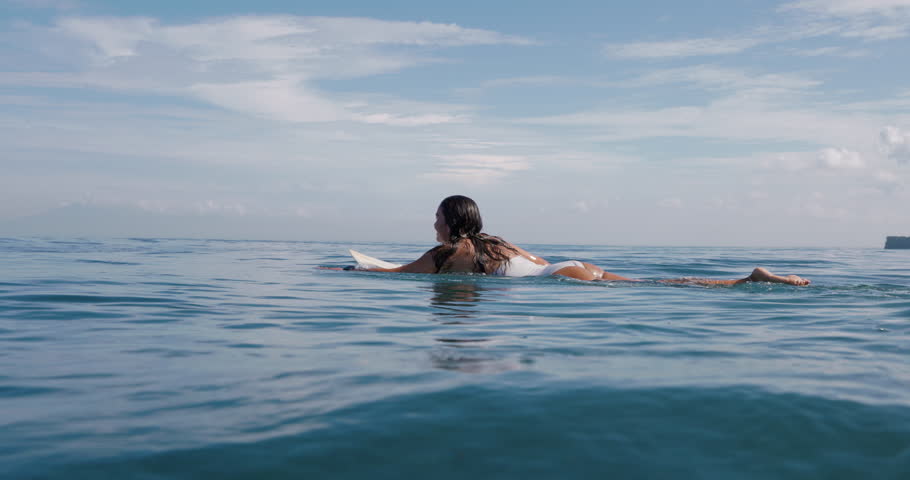Surfer woman on surfboard in blue ocean.