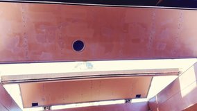 High-angle wide shot of a crew member cleaning the massive interior of a cargo hold on a bulk carrier ship. The video begins by looking up at the heavy steel hatch covers in the open position, allowing natural sunlight to flood the deep red-painted industrial space. The camera slowly tilts down to reveal the sheer scale of the cargo hold, highlighting the structural frames, ribs, and bulkheads. At the bottom, a lone worker clad in an orange safety coverall is seen washing the tank top (floor) with a high-pressure hose. This footage perfectly illustrates the labor-intensive process of maritime maintenance and the preparation required between voyages to ensure the vessel is ready for new freight. It captures the vastness of modern engineering compared to the human figure working within it. - Powered by Shutterstock - Get 15% off with code: PIKWIZARD15