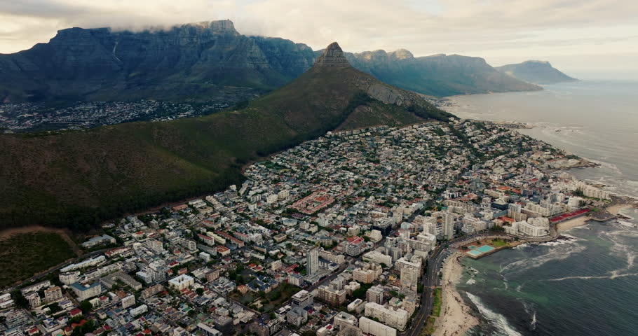 Cinematic aerial view of Cape Town urban infrastructure and rooftops in South Africa. City blocks, coastal skyline and Lions Head peak in soft daylight. Smooth 4K drone flyover establishing shot