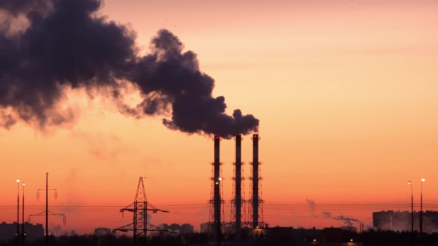 Industrial smokestacks release thick pollution plume over urban city skyline at sunset, highlighting fossil fuel emissions.