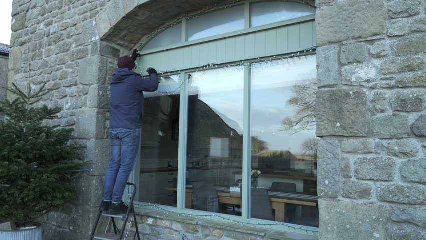 4K: A Man taking down Outdoor Christmas Lights froma Window in January using a stepladder. Stock Video Clip Footage.