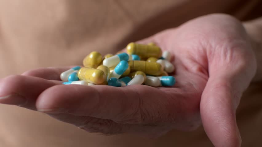 Hand holds mixed capsules and tablets, highlighting supplement overdose risk and confusion between vitamins and medicine.