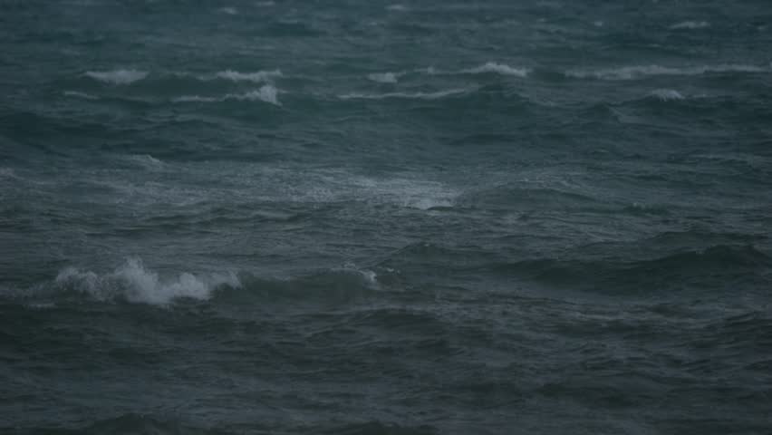 Rough ocean waves rolling in slow motion after sunset with visible wind impact and pre storm atmosphere during blue hour.