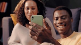 Happy young mixed-race couple sitting on a sofa and making a video call to relatives on a smartphone - Powered by Shutterstock - Get 15% off with code: PIKWIZARD15