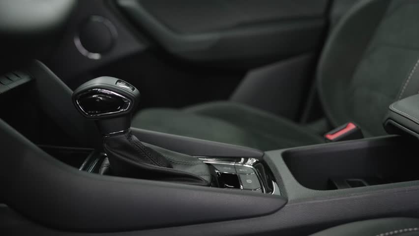 Close-up of a contemporary vehicle interior showing the automatic transmission gear selector, center console, and dark fabric front seats