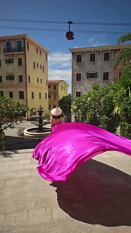 A woman in a bright pink dress poses against the backdrop of a European-style city, a girl in a dress with a long train, flying trail. A beautiful city in an old colonial style, Venice, the Venice of Vietnam