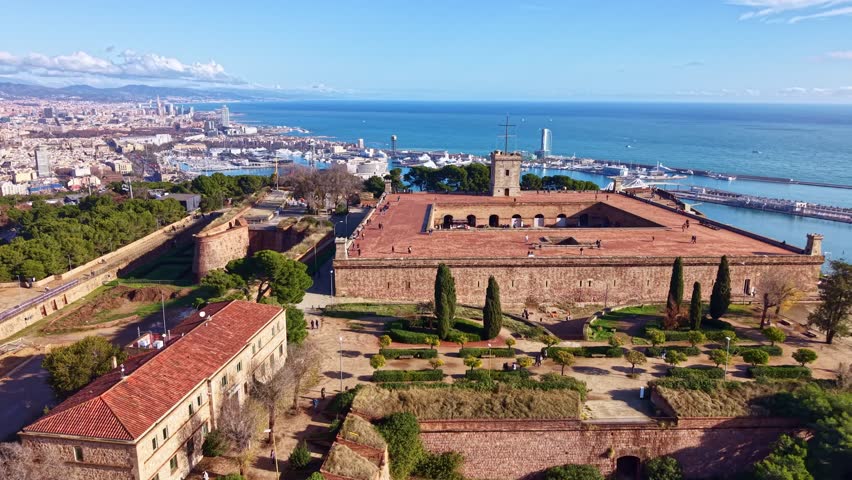 Aerial of Montjuic castle overlooking Barcelona with historic stone walls and coastal cityscape, tracking right establish