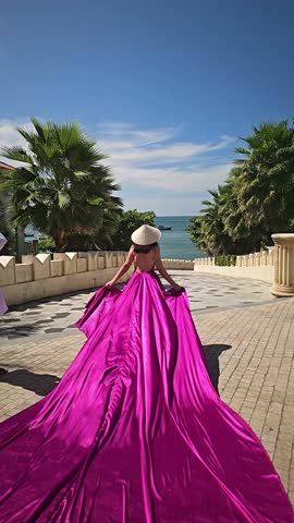A woman in a bright pink dress poses against the backdrop of a European-style city, a girl in a dress with a long train, flying trail. A beautiful city in an old colonial style, Venice, the Venice of Vietnam