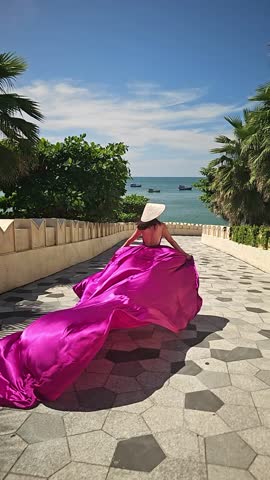 A woman in a bright pink dress poses against the backdrop of a European-style city, a girl in a dress with a long train, flying trail. A beautiful city in an old colonial style, Venice, the Venice of Vietnam