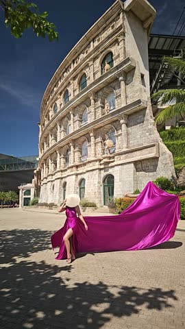 A woman in a bright pink dress poses against the backdrop of a European-style city, a girl in a dress with a long train, flying trail. A beautiful city in an old colonial style, Venice, the Venice of Vietnam