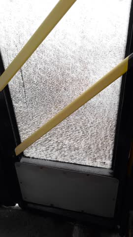 Frosted dirty bus door window with yellow handrails inside public transport.