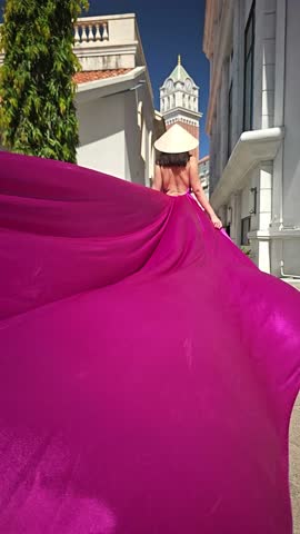 A woman in a bright pink dress poses against the backdrop of a European-style city, a girl in a dress with a long train, flying trail. A beautiful city in an old colonial style, Venice, the Venice of Vietnam