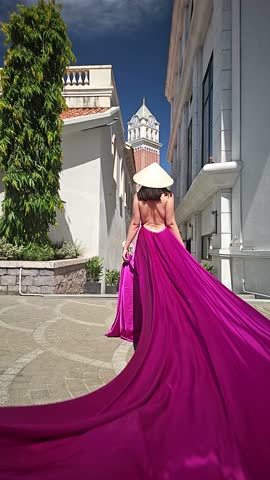 A woman in a bright pink dress poses against the backdrop of a European-style city, a girl in a dress with a long train, flying trail. A beautiful city in an old colonial style, Venice, the Venice of Vietnam