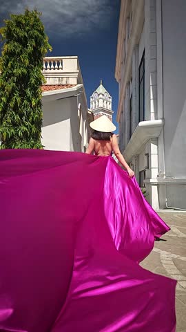 A woman in a bright pink dress poses against the backdrop of a European-style city, a girl in a dress with a long train, flying trail. A beautiful city in an old colonial style, Venice, the Venice of Vietnam