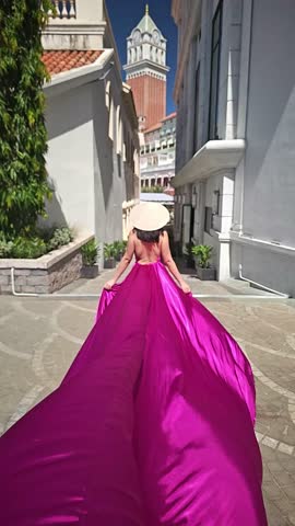 A woman in a bright pink dress poses against the backdrop of a European-style city, a girl in a dress with a long train, flying trail. A beautiful city in an old colonial style, Venice, the Venice of Vietnam