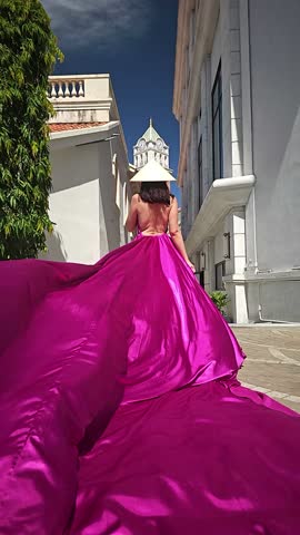 A woman in a bright pink dress poses against the backdrop of a European-style city, a girl in a dress with a long train, flying trail. A beautiful city in an old colonial style, Venice, the Venice of Vietnam