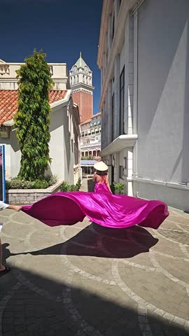 A woman in a bright pink dress poses against the backdrop of a European-style city, a girl in a dress with a long train, flying trail. A beautiful city in an old colonial style, Venice, the Venice of Vietnam