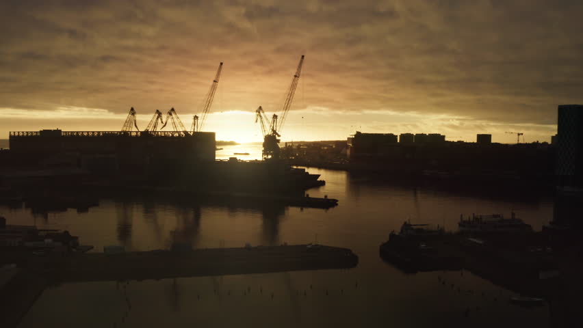 Industrial shipyard cranes silhouette at Helsinki West Harbour during sunset aerial view, Finland maritime logistics and shipping infrastructure scene under dramatic autumn sky at dusk.