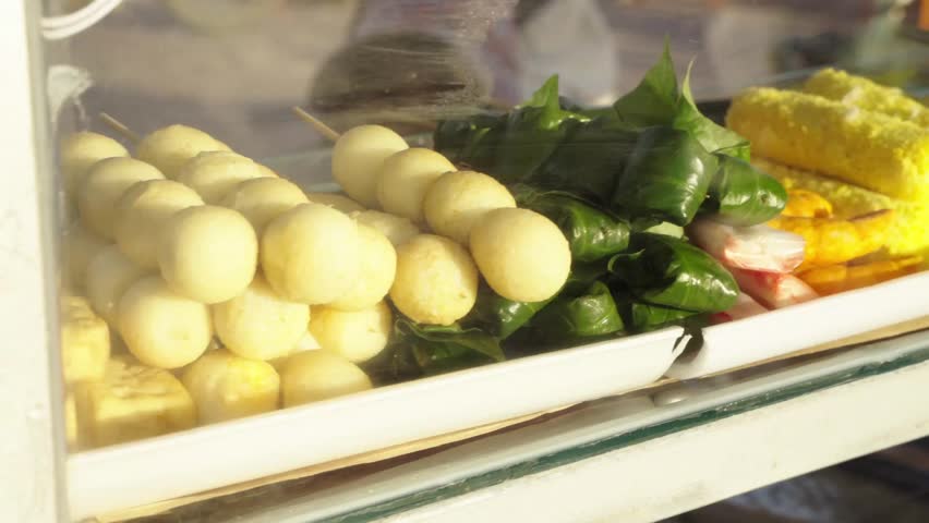 Traditional Vietnamese street snacks and colorful local treats arranged on trays in a street food stall, close view through a glass display case.
