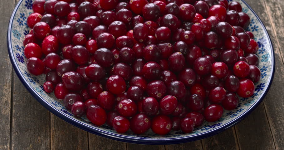A heap of fresh cranberries displayed on a decorative platter set against a rustic wooden background, table spin.