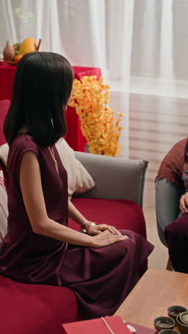 Vertical shot of two young Asian women exchanging boxes with presents while gathering at home for Tet celebration