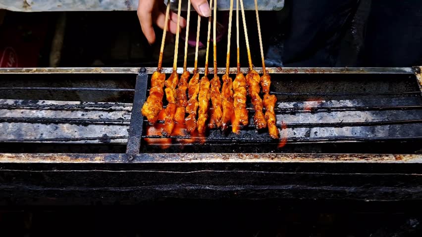 Chicken satay skewers are being grilled over an open flame on a traditional barbecue.