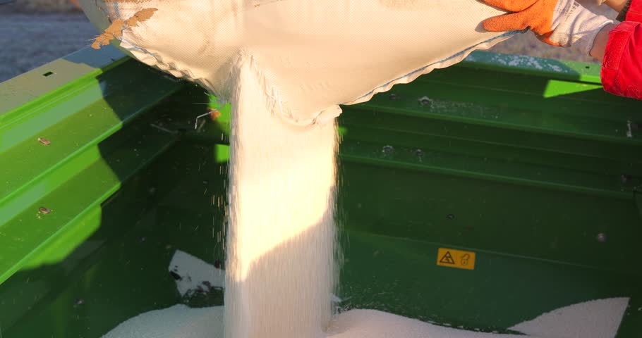 Pouring mineral fertilizer in granules into the fertilizer spreader. Farmer pouring fertilizer from large sacks. Proper growth and development of plants requires a balance of nutrients found in the soil
