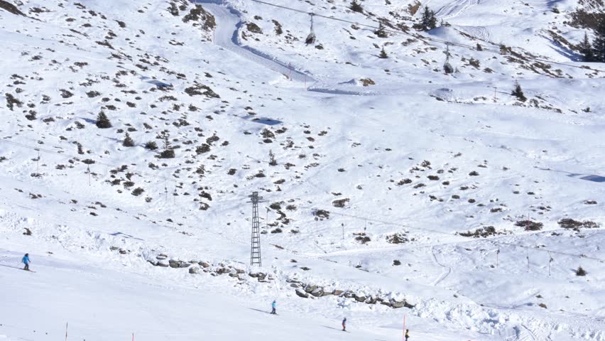 Skiers descending a wide, groomed piste in a beautiful mountain resort on a sunny winter day