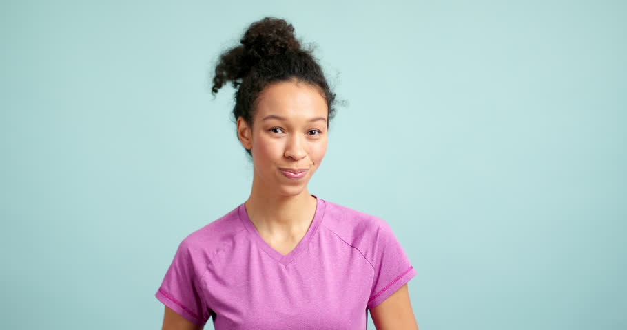 Positive young woman showing a thumbs up gesture and smiling at the camera over a blue background