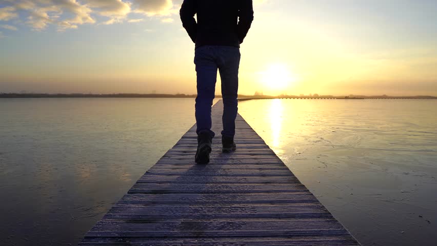 A man walking on a jetty (Knuppelpad) in nature reserve Roegwold during a cold, foggy sunrise.
