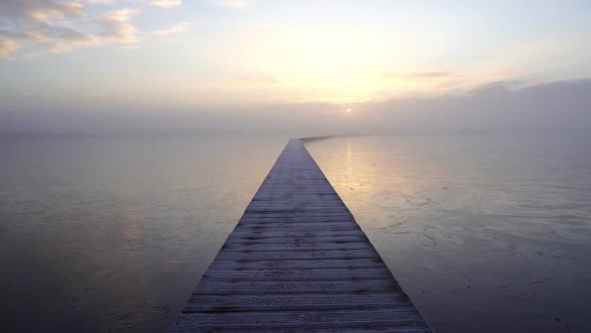 A man walking on a jetty (Knuppelpad) in nature reserve Roegwold during a cold, foggy sunrise.