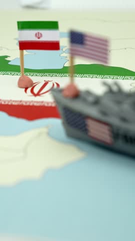 Plastic toy warship with an american flag approaching the coast of Iran on a political map, representing a conceptual military conflict, tension and diplomatic crisis between nations