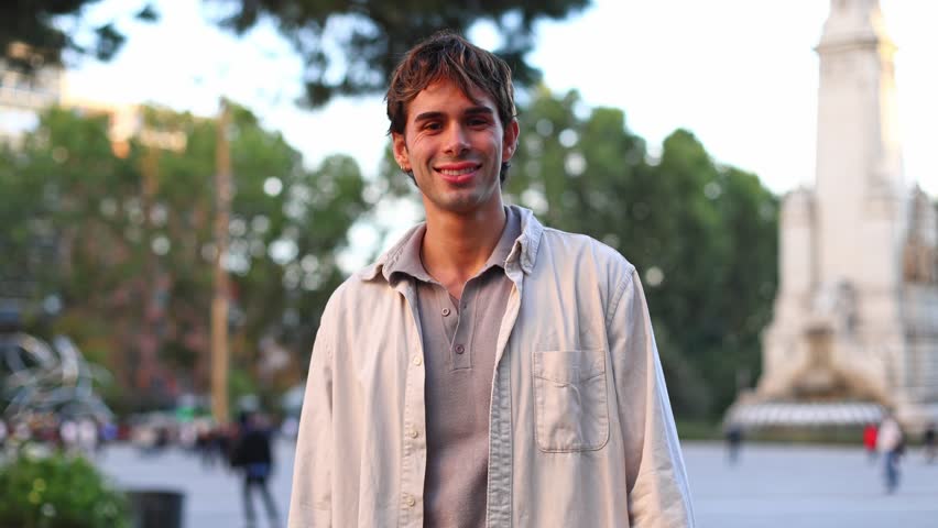 Portrait of a confident and happy young man smiling at the camera. He is standing in a city square with a warm sunset light on his face