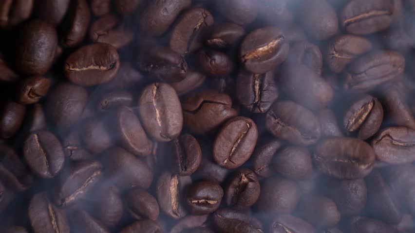 Close up of seeds of coffee. Fragrant coffee beans are roasted smoke comes from coffee beans, with cup coffee