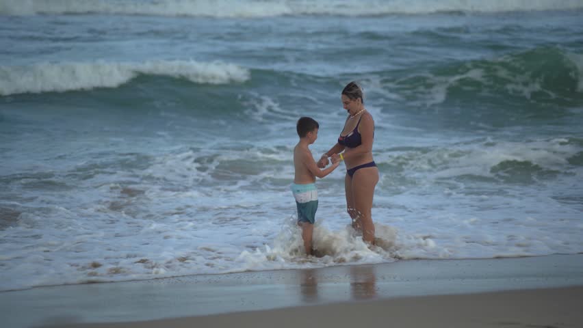 Mother and son wrestle and have fun with the sea waves together, holding hands