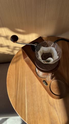 Top view pouring water from black kettle in v60 paper filter with fresh grind coffee beans on the wooden table in cafe or at home