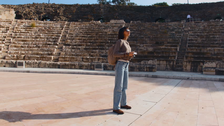 A tourist photographs an ancient amphitheater. A young woman travels and enjoys her vacation. A young woman photographer. Creating content for a blog. Travel and adventure.