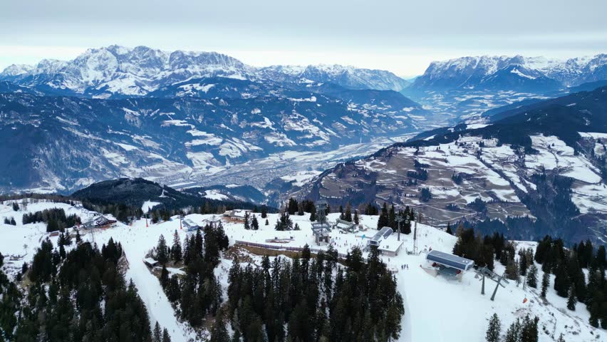 Breathtaking aerial view of a vibrant Austrian snow space ski resort, nestled amidst majestic snow-capped Alps under a soft winter sky.