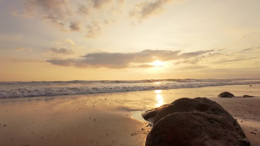 Golden sunset over a tropical beach with waves and rocks