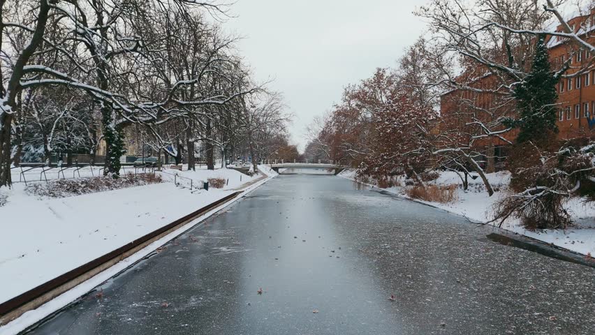 Winter drone aerial view of the Körös Canal in downtown Békéscsaba, Hungary, covered in snow in 4k.