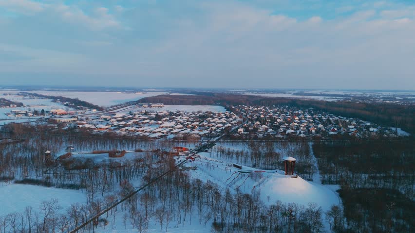 Winter drone aerial view of the CsabaPark lookout tower and surrounding forest in Békéscsaba, Hungary, covered in snow in 4k.