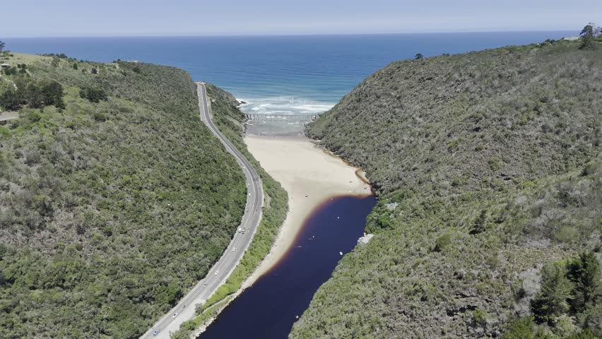 Drone flies southeast over partially dried up Kaaimans River on sunny day on the Garden Route in Wilderness, South Africa