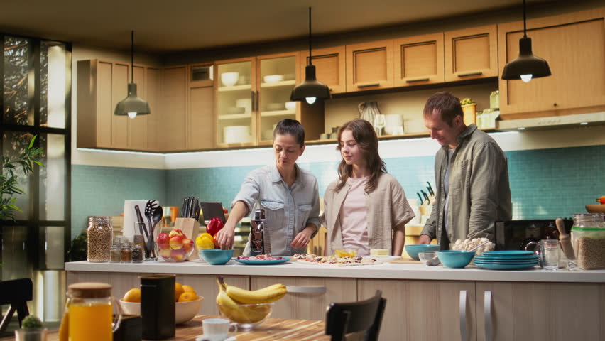 Mother takes selfies on phone while they cook delicious homemade pizza together in kitchen, daughter enjoying laughter and the warmth of family bonding with her parents. Camera A.