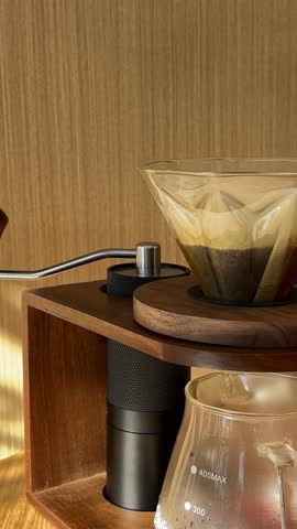 Close-up of pouring water from black kettle in v60 paper filter with fresh grind coffee beans on the wooden table in cafe or at home