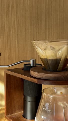 Close-up of pouring water from black kettle in v60 paper filter with fresh grind coffee beans on the wooden table in cafe or at home