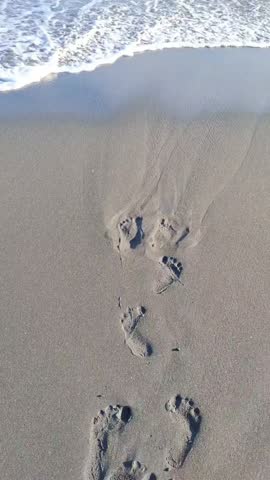 Vertical Top View of Ocean Waves Washing Away Footprints on Sandy Beach