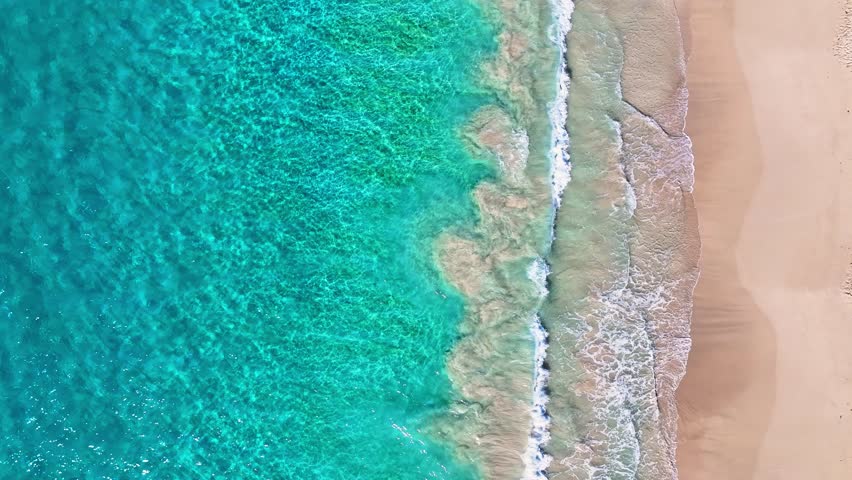 A beautiful view of a beach with calm ocean waves, seen from a drone. A picturesque view of a stunning landscape. White waves of a turquoise sea on yellow sand. A sea bay with blue water.