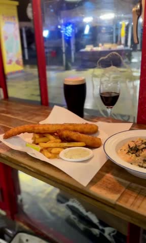 Crispy fish and chips with salmon pasta on a plate, served in a rustic British-style restaurant.
