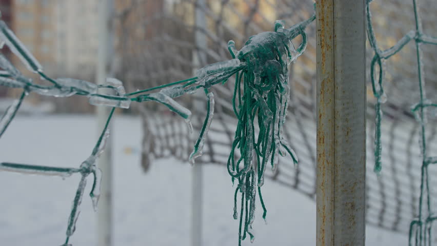 Close-up of a green soccer goal net frozen solid with layers of ice and icicles, showing harsh winter weather conditions.