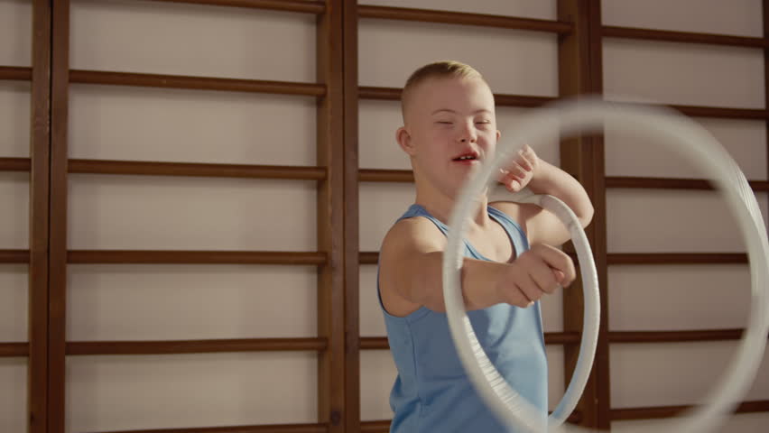 Boy with Down syndrome spinning gymnastic hoop on his arm while practicing in inclusive sports class focused on coordination, motor skills physical activity
